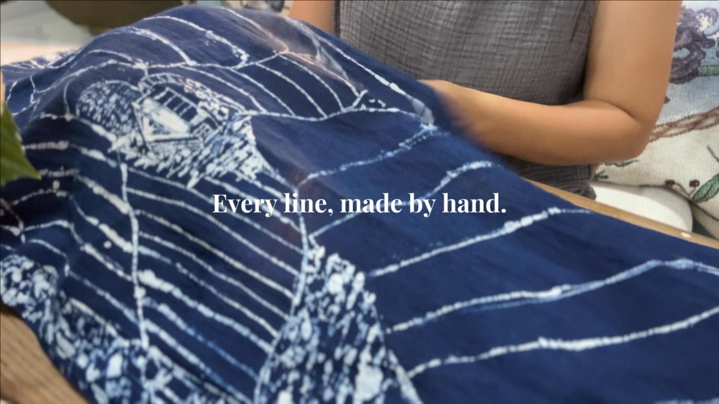 Tấm khăn chàm vẽ sáp hình ngôi nhà và ruộng bậc thang, dòng chữ Every line, made by hand